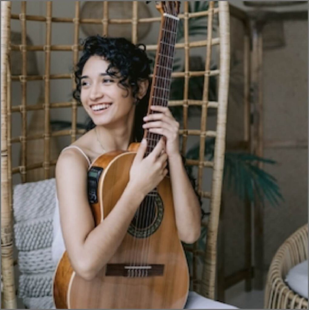 A woman is smiling and holding a guitar upright